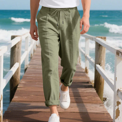 Man walking on pier wearing army green American Linen men's casual pants, perfect for summer leisure activities by the beach.