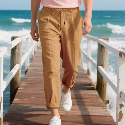 Man walking on pier in light brown casual linen pants, perfect for summer leisure. Mid-waist drawstring style.