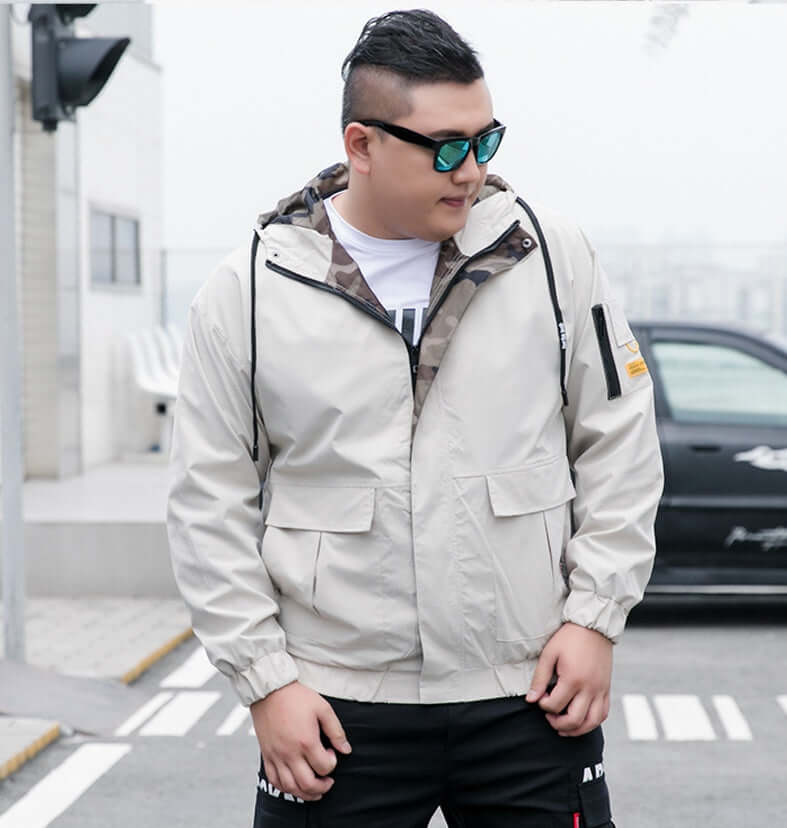 Man wearing a stylish beige bomber jacket with camouflage hood in urban setting.