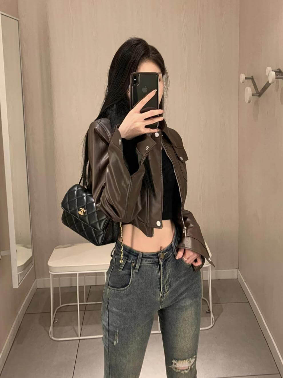 Woman wearing a stylish coffee color leather motorcycle jacket with flying sleeves, paired with jeans and a chic handbag.