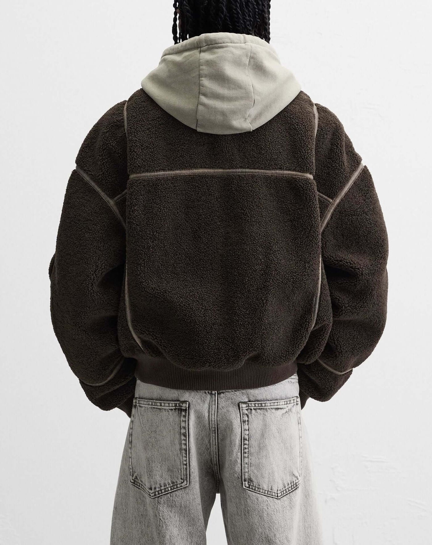 Back view of a casual men's fleece jacket in dark brown with a light gray hood, styled with gray jeans.