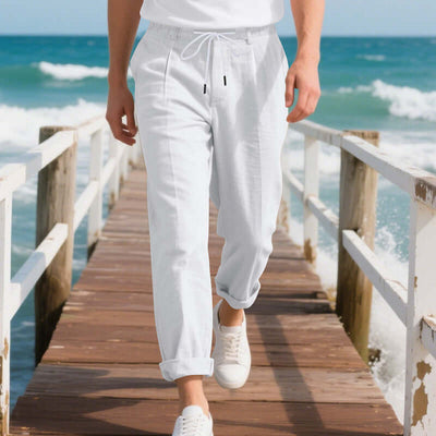 Man walking on a beach pier in white American linen casual pants, showcasing a relaxed summer style.