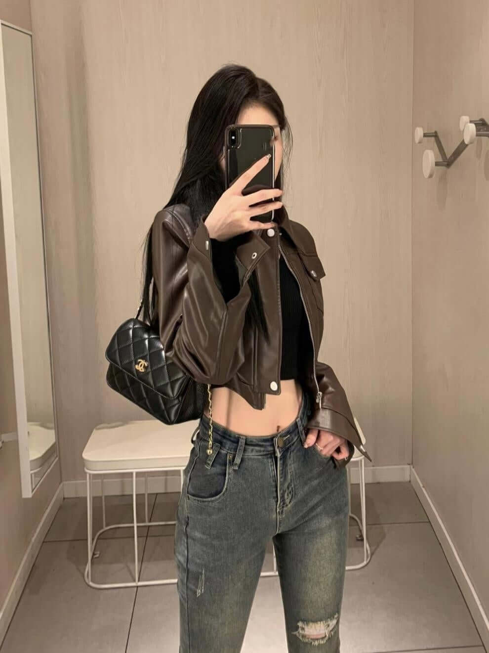 Stylish woman wearing a coffee color leather motorcycle jacket with super long sleeves in a modern setting.