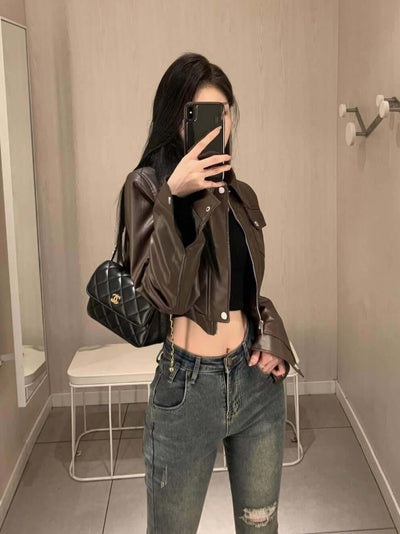 Stylish woman wearing a coffee color leather motorcycle jacket with super long sleeves in a modern setting.