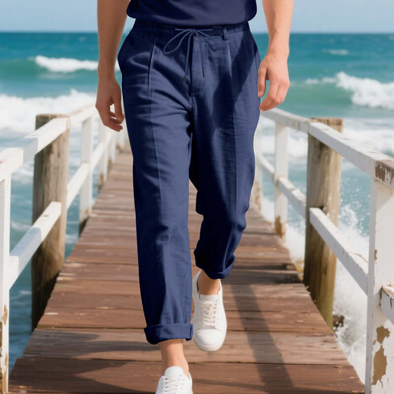 Men's navy linen casual pants, summer loose straight style, walking on a pier by the sea.
