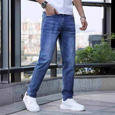 Men's light blue stretch slim jeans in urban setting, paired with white sneakers, showcasing a stylish and casual look.
