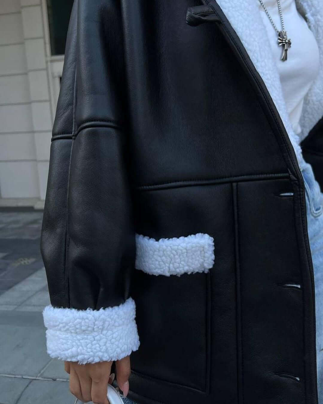 Close-up of a black leather and white fur splicing coat with long sleeves and pockets, perfect for women.