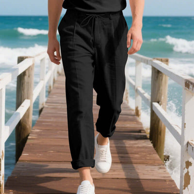 Man wearing black linen casual pants walking on a pier by the ocean, perfect for summer leisure activities.