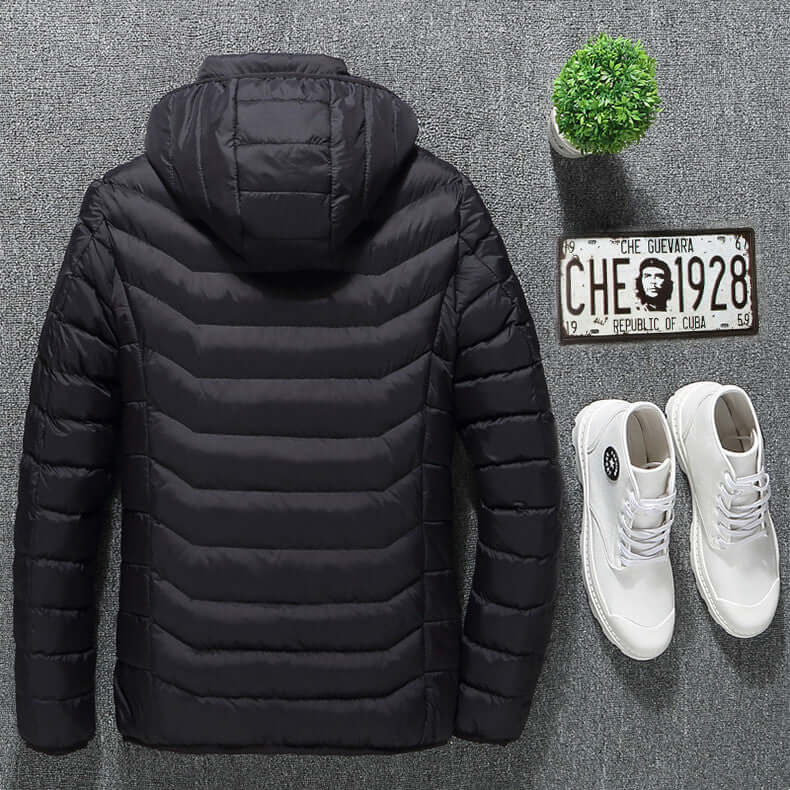 Black heated jacket with removable hood, lightweight design, paired with white sneakers and a small plant.