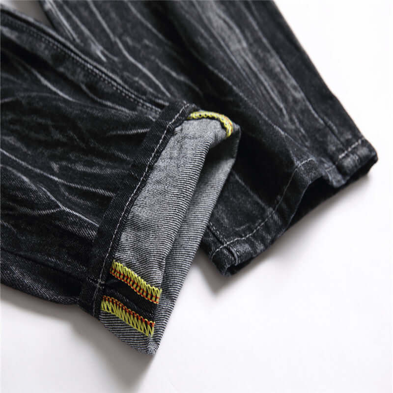 Close-up of the hem and stitching details of men's black decorative flower ripped straight jeans.