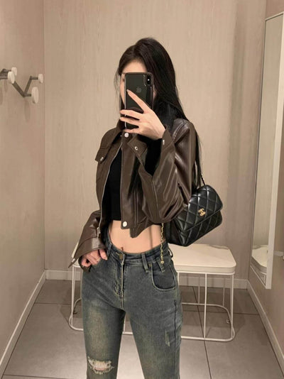 Stylish woman in a brown leather motorcycle jacket paired with high-waisted jeans and a handbag in a modern setting.