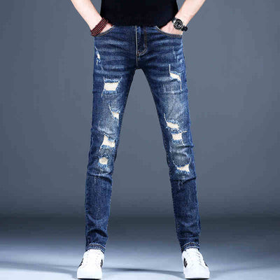 Men's ripped skinny jeans in dark blue denim with distressed detailing, styled casually with white sneakers.